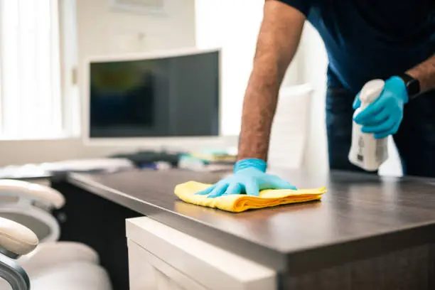 Office cleaner sanitizing conference room table before morning meetings in busy Farmers Branch workspace